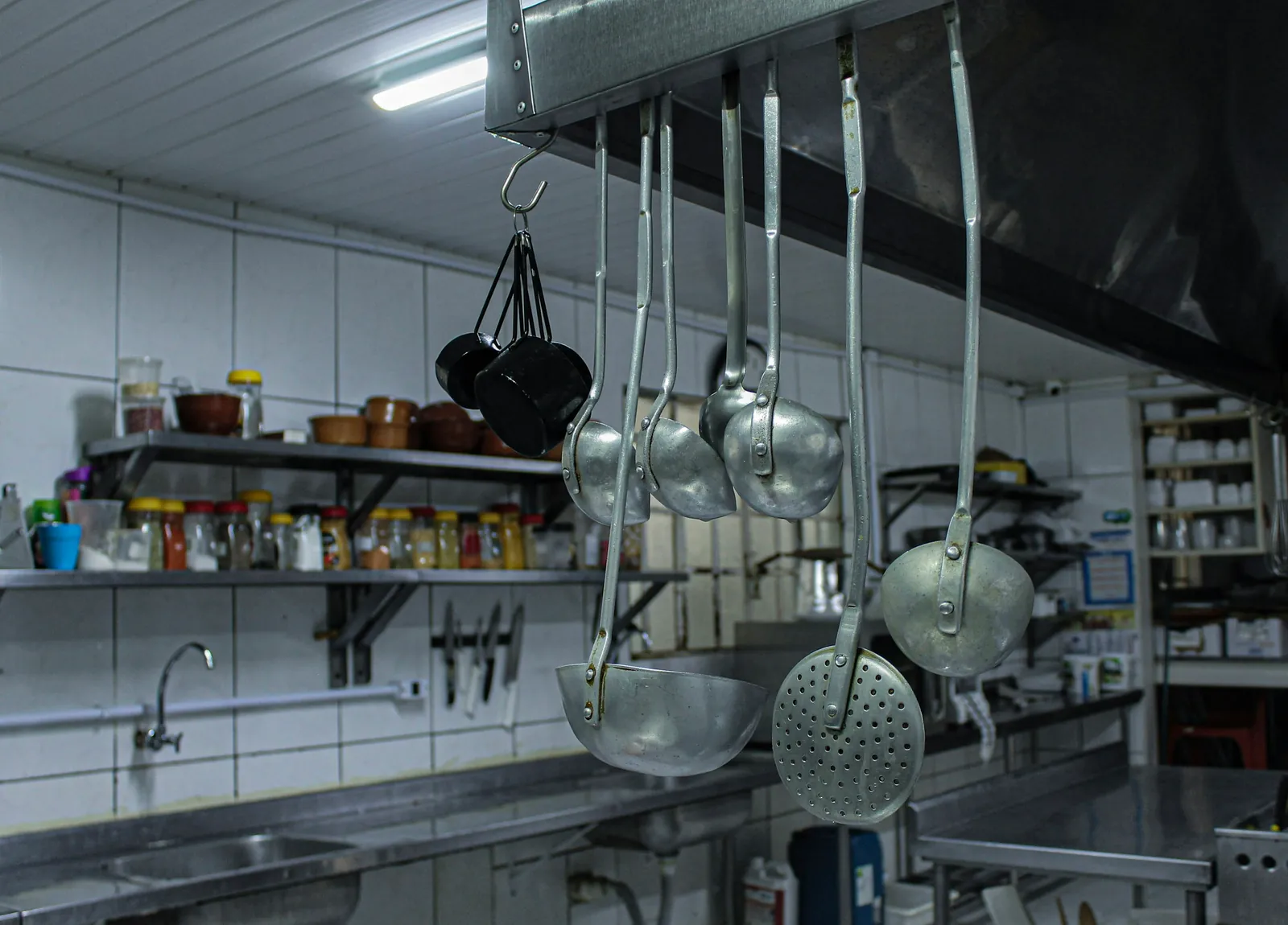 A restaurant kitchen with steel counters, open shelves and tiled walls.
